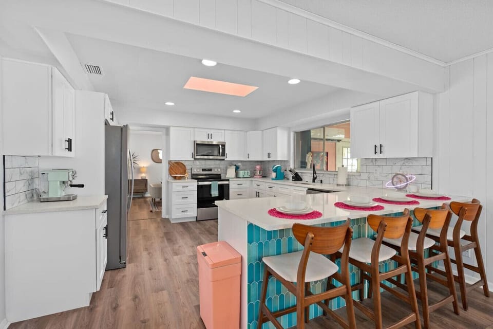 Retro-chic kitchen with white cabinets, wood dining table, colorful teal and pink mid-century chairs and stainless appliances, Vivid Vintage Orlando