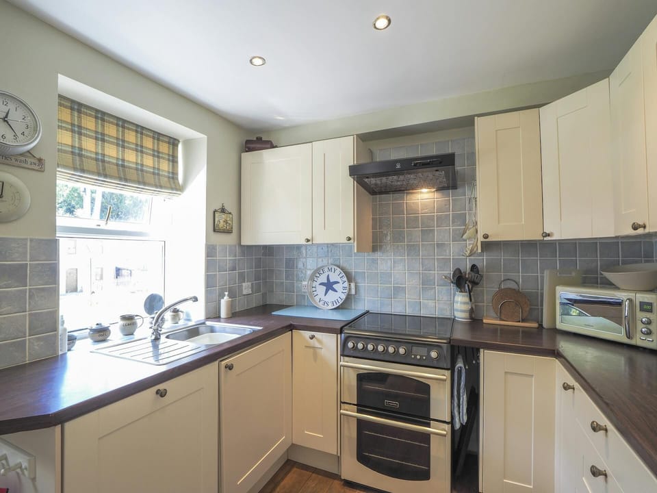 Kitchen showing cooker, sink by the window, units, wall clock and microwave