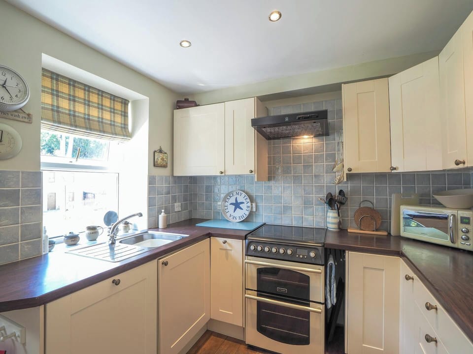 Kitchen showing cooker, sink by the window, units, wall clock and microwave