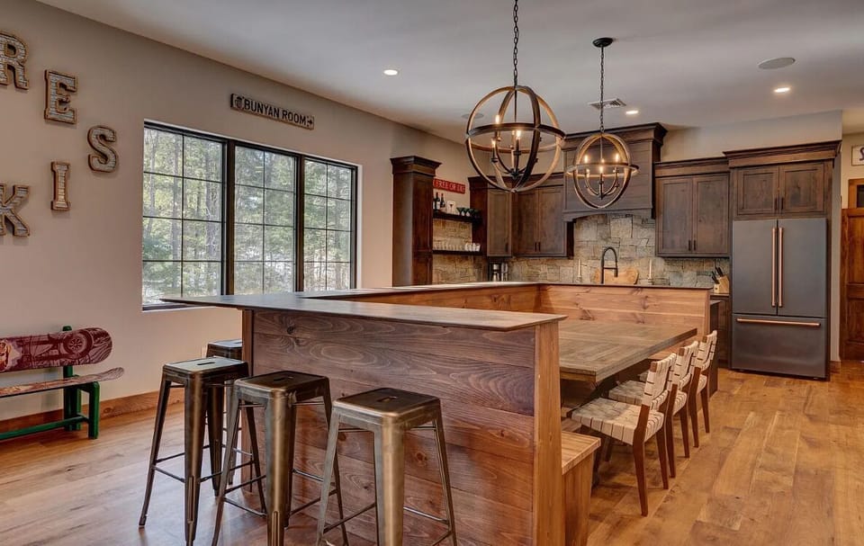 Charming kitchen with warm wood finishes, stone accents, and stylish globe pendant lights. Features a spacious breakfast bar with ample seating, perfect for enjoying meals or gathering with family.