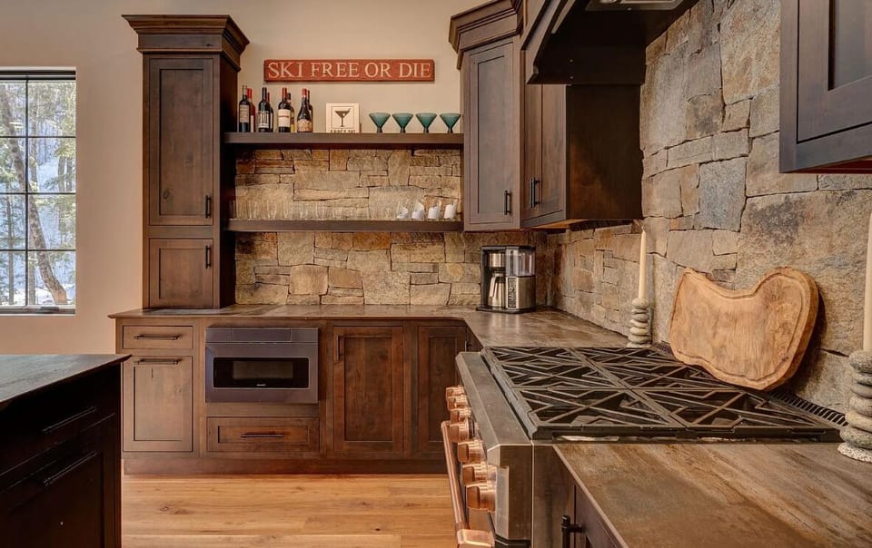 Elegant kitchen with custom wood cabinetry, stone backsplash, and a high-end gas range. Open shelving and charming decor create a warm, inviting space, perfect for preparing meals during your stay.