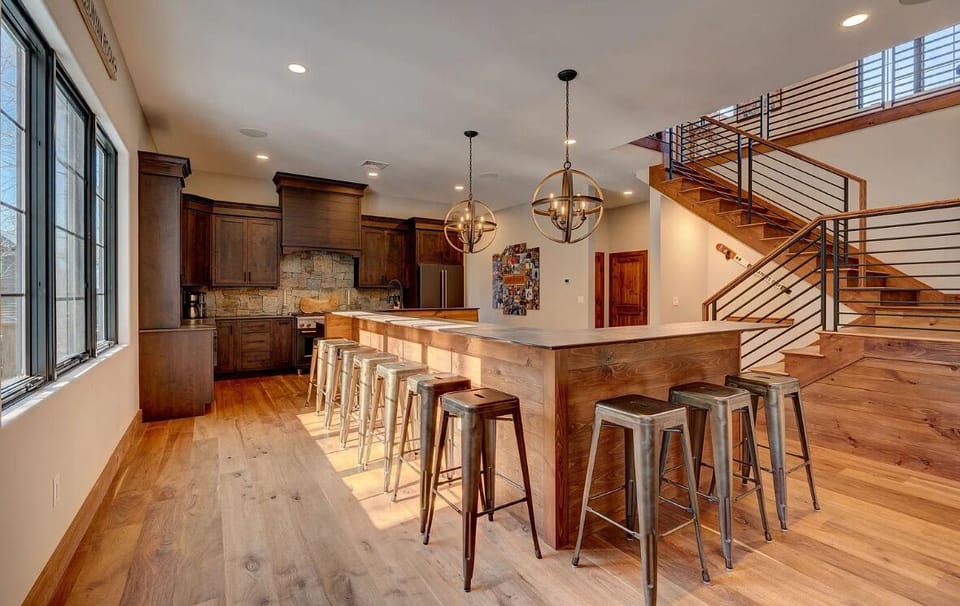 Spacious kitchen with a large island and ample seating, perfect for entertaining. The modern design features rustic wood elements, globe pendant lights, and a beautiful stone backsplash, creating a warm and inviting atmosphere.