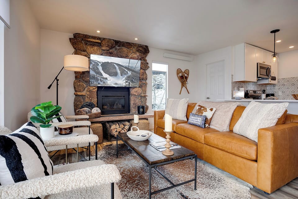 Cozy up in your stylish living room with a crackling stone fireplace, plush leather seating, and mountain views on the wall-mounted TV.