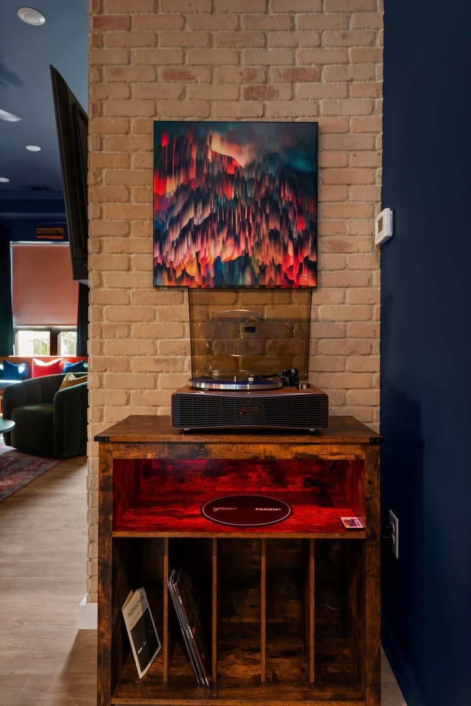 A cozy corner with a vintage record player, set against a brick accent wall, complete with vibrant artwork and a vinyl storage space that adds to the room’s artistic charm.