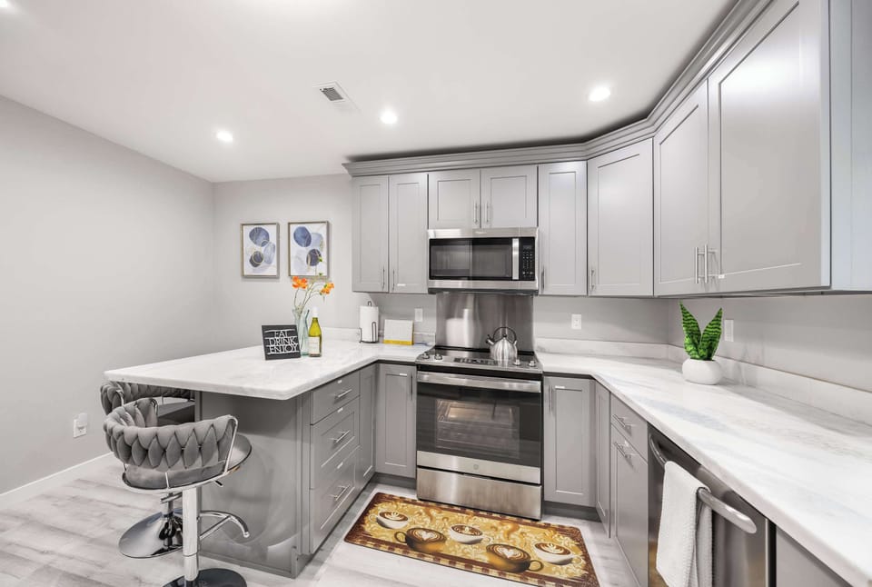 "Bright and inviting kitchen featuring stainless steel appliances, modern gray cabinetry, and marble countertops. The cozy breakfast nook and vibrant decor make it an ideal spot to enjoy meals or morning coffee.