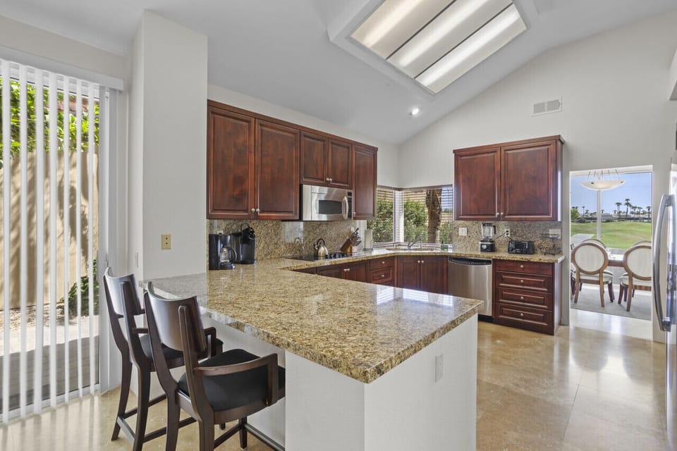 Spacious kitchen w/ granite counters, bar seating & rich wood cabinetry under skylights
