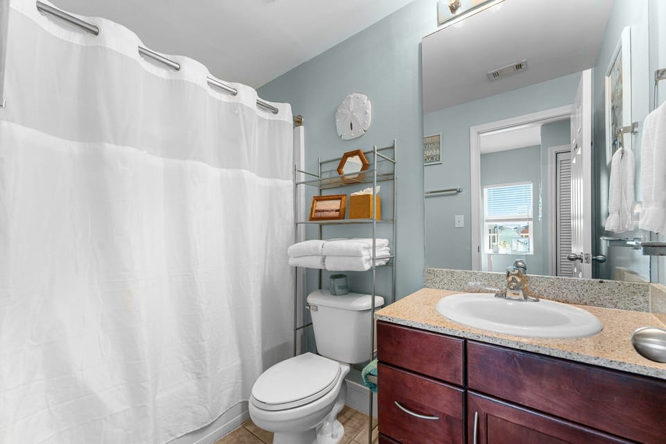 Modern bathroom with a shower curtain, storage rack, and granite countertop.