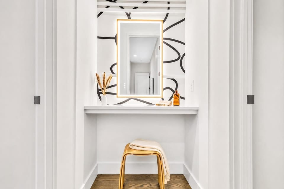 Bathroom vanity with a stool and mirror tucked into the corner, creating a compact prep zone before heading downstairs