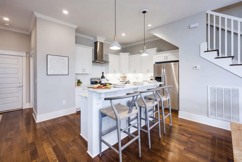 The kitchen island is made for cooking together: three stools pull up, the open layout keeps the cook in the conversation, and the group eats as one crew