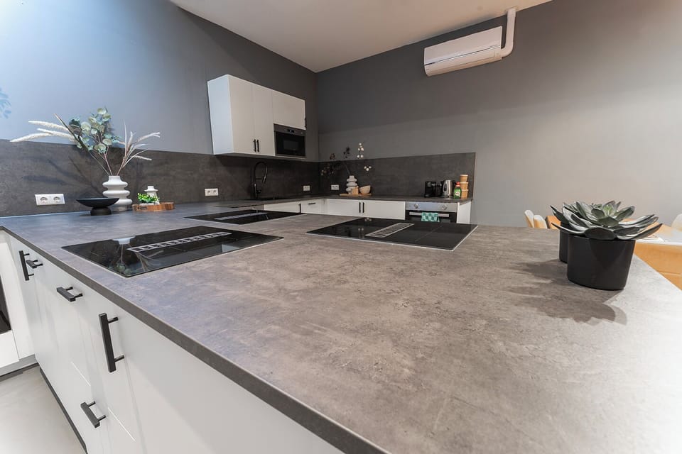 Under a dramatic angular ceiling with skylights, this kitchen combines contemporary white cabinets and bold dark countertops, creating a striking yet inviting atmosphere.
