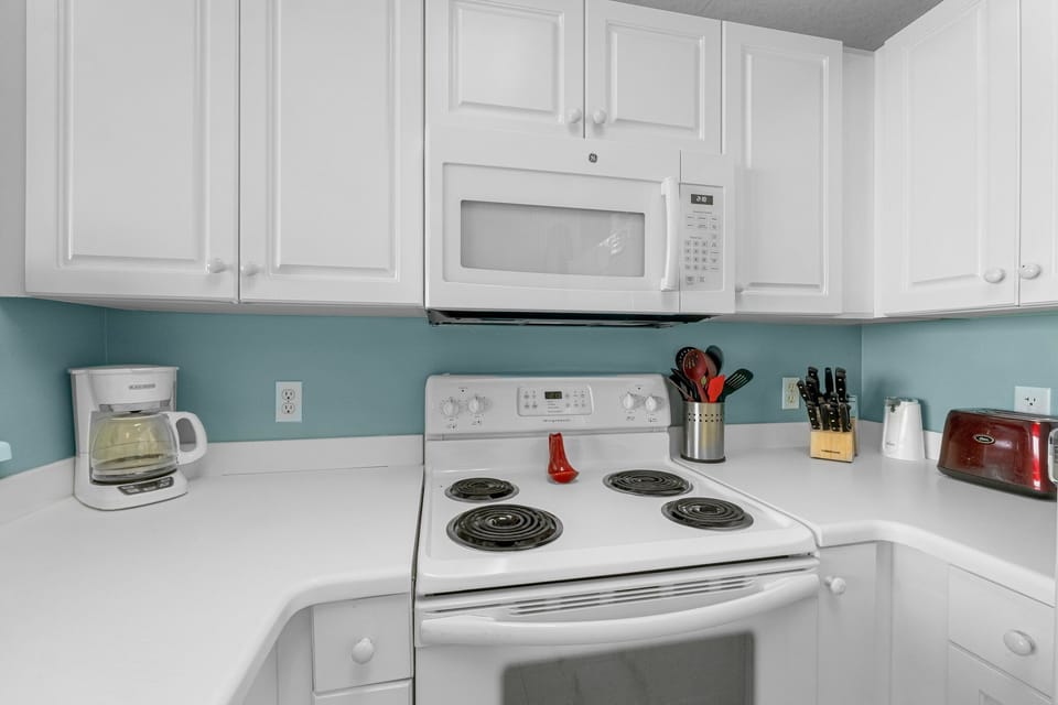 Compact kitchen with electric stove and white cabinetry against a soft blue backsplash
