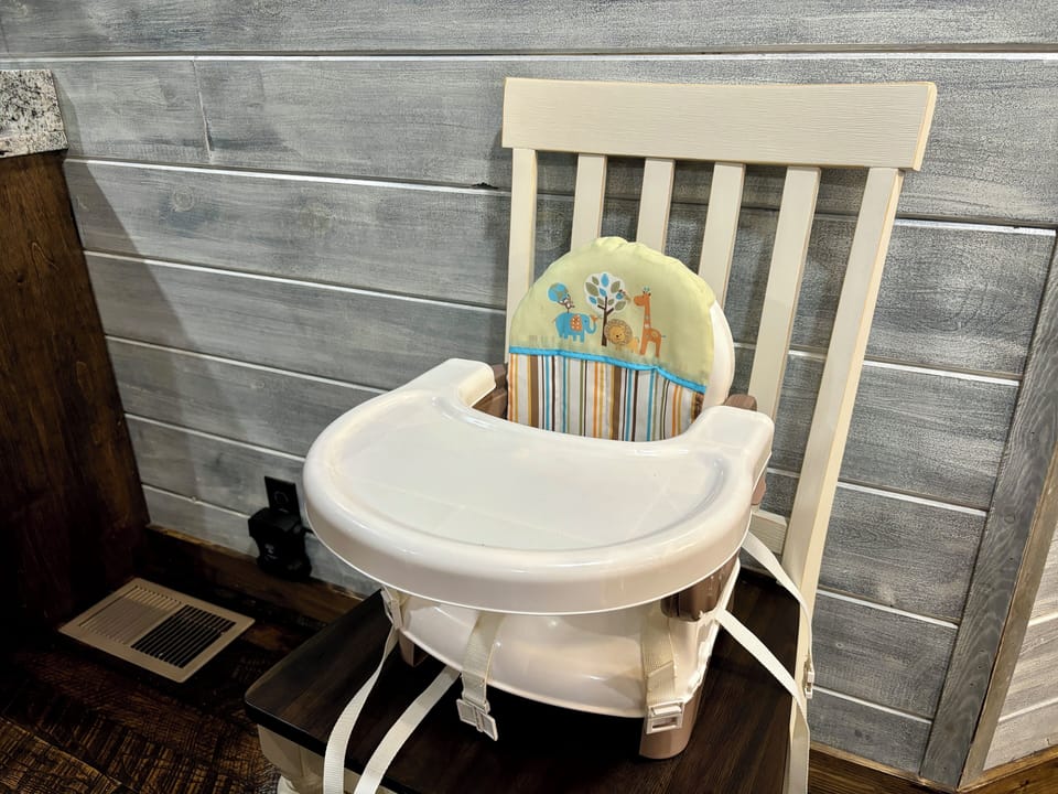 Infant high chair with animal prints, secured to wooden chair for easy mealtime.