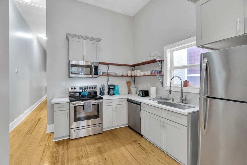 Modern and fully equipped kitchen, featuring stainless steel appliances and open shelving with all the essentials. Ideal for home-cooked meals or a quick coffee before exploring New Orleans!