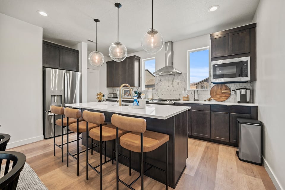 The gourmet kitchen features an island with seating for four and is equipped with brand-new stainless steel appliances, including a microwave, gas stove, and spacious refrigerator.