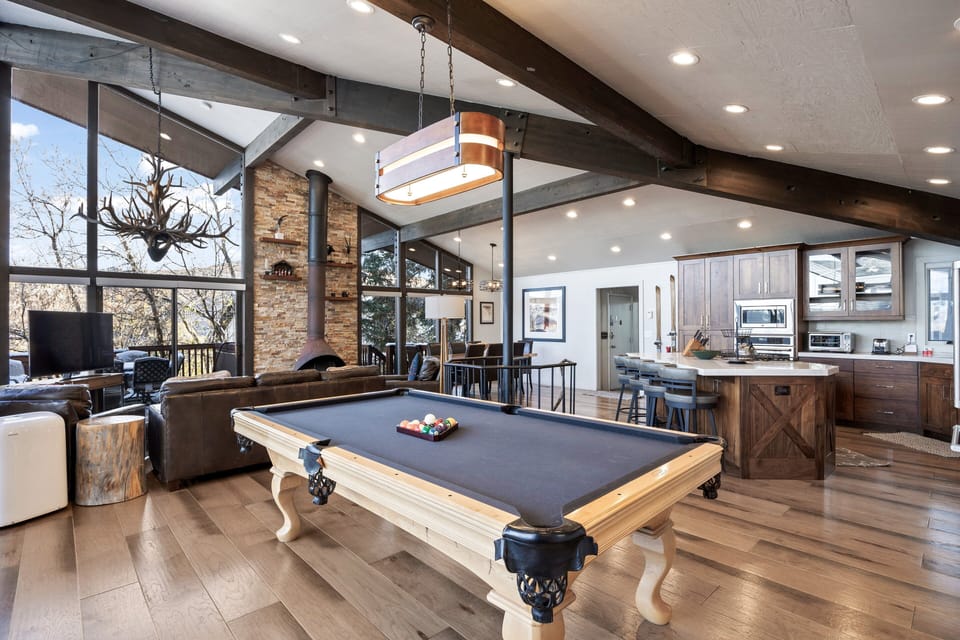 - Open layout with pool table and rustic fireplace framed by mountain views  
- Leather seating and antler chandelier create inviting mountain style  
- Spacious kitchen and living room perfect for family gatherings