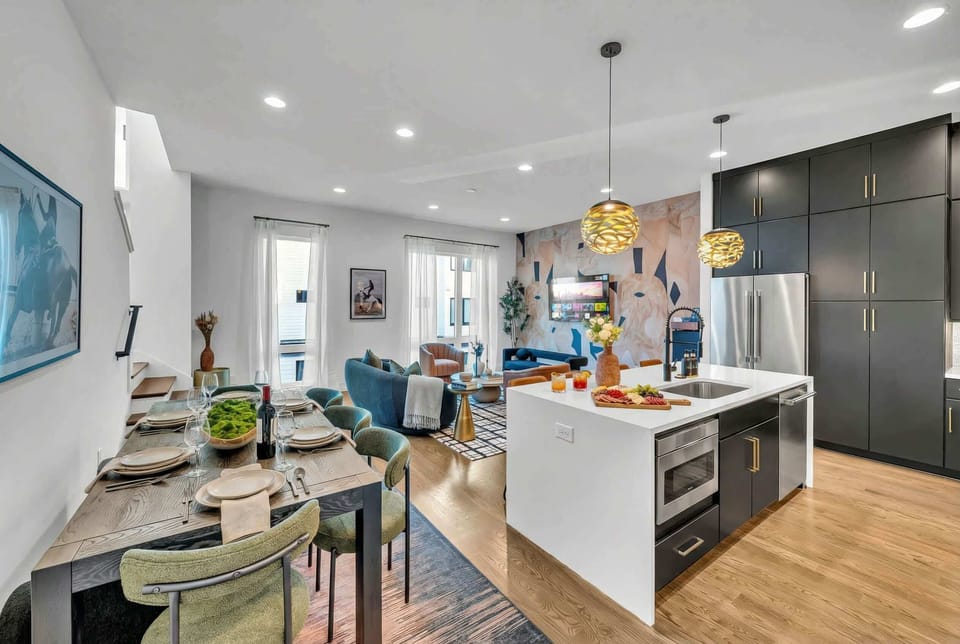 Dining and living merge into one sprawling open-plan zone anchored by a wooden table that seats the whole crew, with the kitchen island visible just beyond