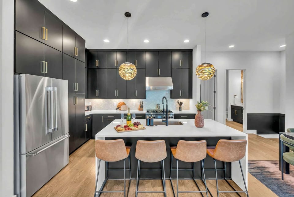 The kitchen features stainless steel appliances, a gas stove, and an island with bar stools under gold pendant lights so the cook stays connected to the group
