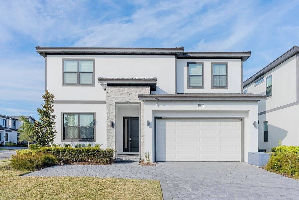This contemporary home boasts a striking white exterior with dark trim and large windows that fill the space with natural light. The well-kept lawn and welcoming entrance create the perfect setting for a relaxing stay inside.