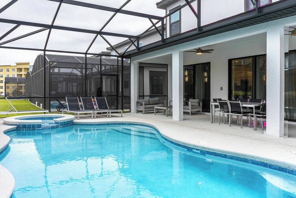 Step outside to a bright pool area, featuring a sparkling blue pool framed by sleek loungers and a shaded dining spot. The screened enclosure ensures comfort while you enjoy the sun or relax with a refreshing drink.