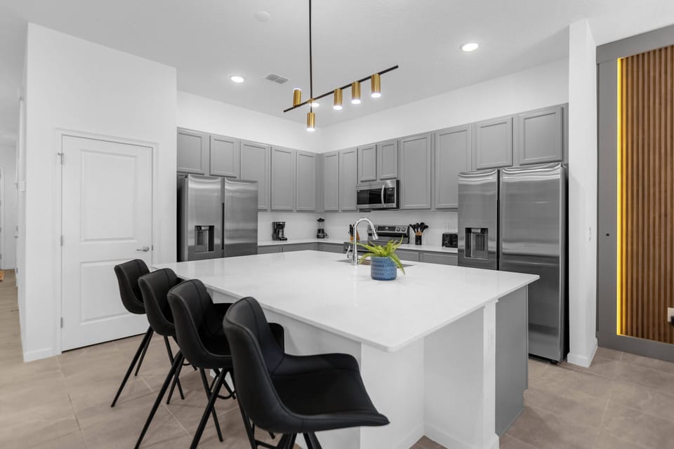 Enjoy a chic kitchen with sleek gray cabinets and modern stainless steel appliances. The spacious island is ideal for casual dining, enhanced by elegant black seating and stylish contemporary lighting for a welcoming atmosphere.
