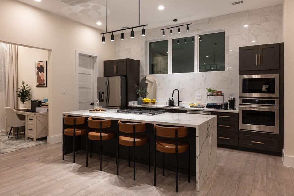 A modern kitchen with a large island, a stainless steel refrigerator, and dark cabinets.