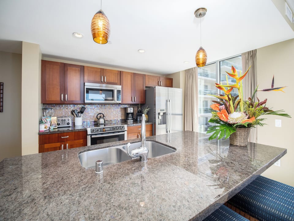 Fully equipped kitchen with granite countertops, modern appliances, and beautiful tropical flowers, ideal for gourmet cooking.