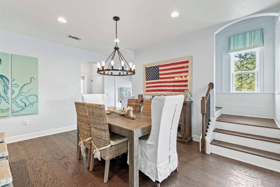 Gather around your rustic dining table beneath a charming chandelier, where patriotic charm meets coastal comfort in this welcoming space.