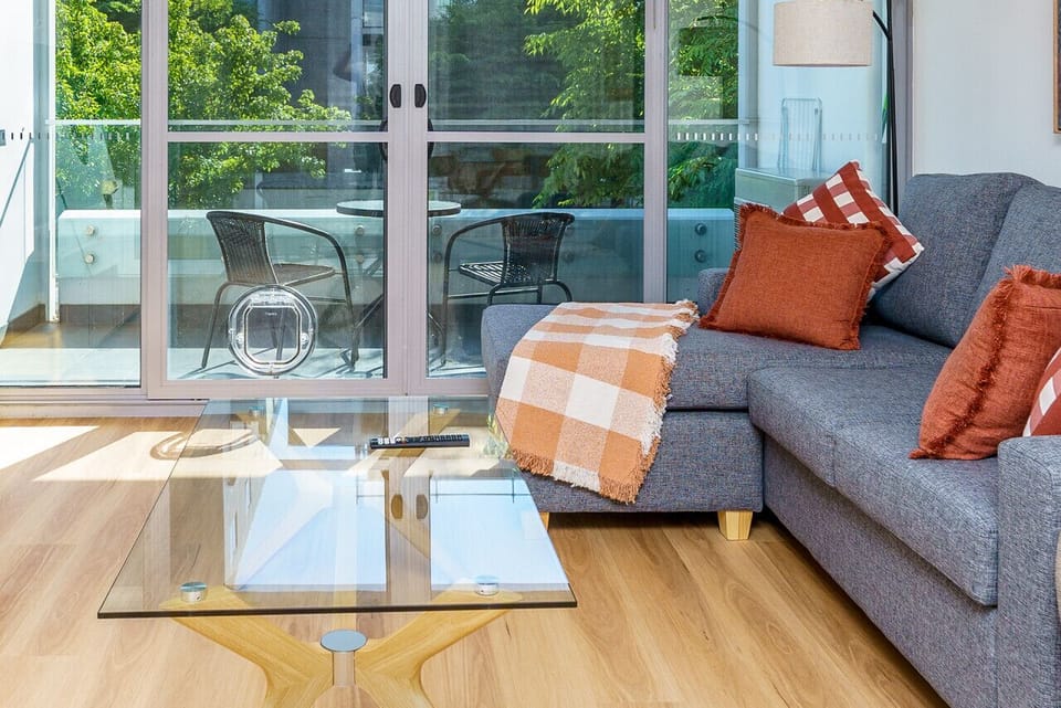 A modern living and dining space with clean, stylish furniture. The dining area features a sleek table and chairs, while the living area includes a comfortable lounge and a smart TV.