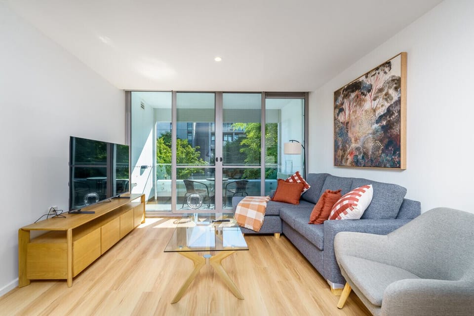 A modern living and dining space with clean, stylish furniture. The dining area features a sleek table and chairs, while the living area includes a comfortable lounge and a smart TV.