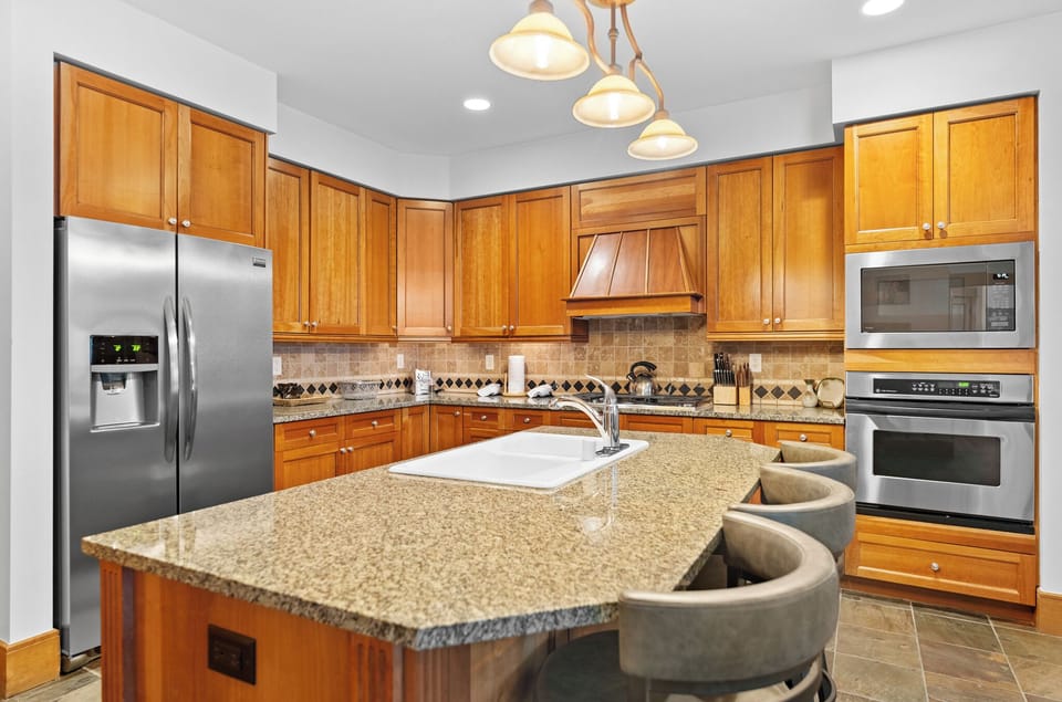 Step into your fully equipped kitchen featuring granite countertops, stainless steel appliances, and warm wood cabinetry for memorable meal preparation.