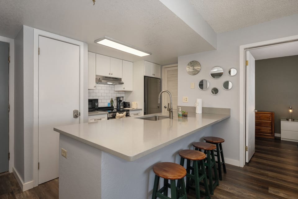 Your modern kitchen at Summit Unit 1103 features bright white cabinets, gleaming countertops, and a breakfast bar where you can start your day with coffee.