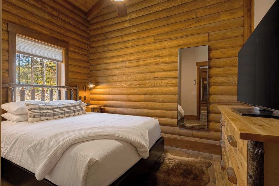 Rest easy in the Double Queen Suite's cozy bedroom, featuring handcrafted log accents, warm lighting, and inviting views of the Smoky Mountains.