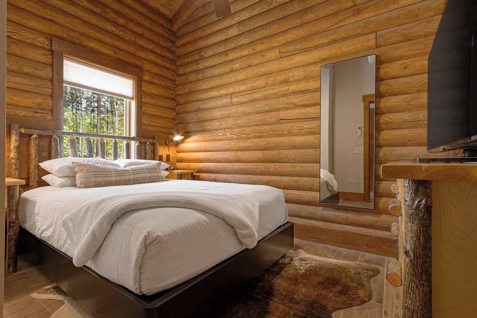 The Queen Room showcases a sleek ash bed frame with handcrafted log accents and plush resort linens for ultimate comfort and style.