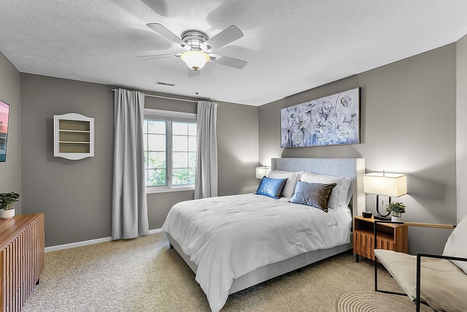 Unwind in your serene bedroom with elegant gray tones, plush bedding, and gentle ceiling fan breeze creating the perfect retreat.