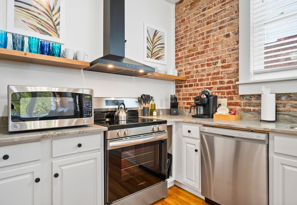The kitchen features sleek appliances, counter space, and exposed brick that combines modern style with rustic charm.