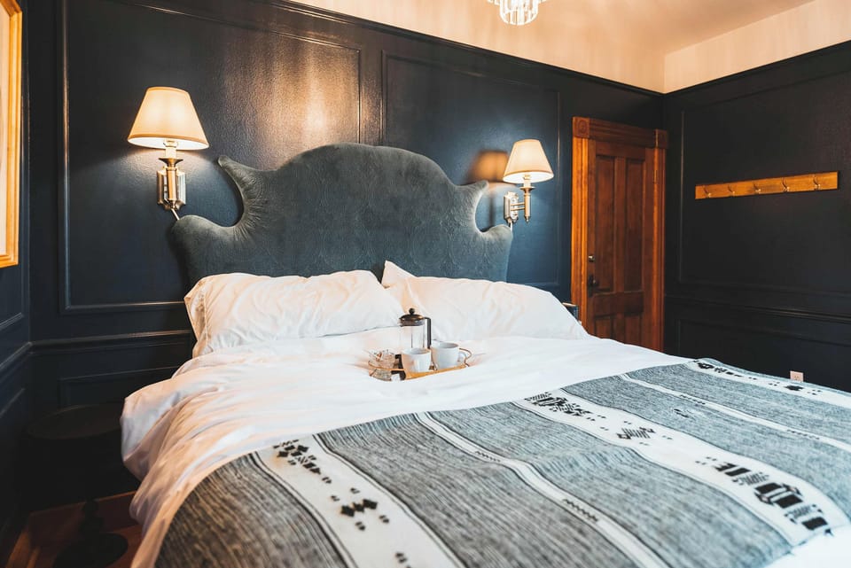 Elegant bedroom with deep blue wainscoting, statement lighting, and original timber doors.
