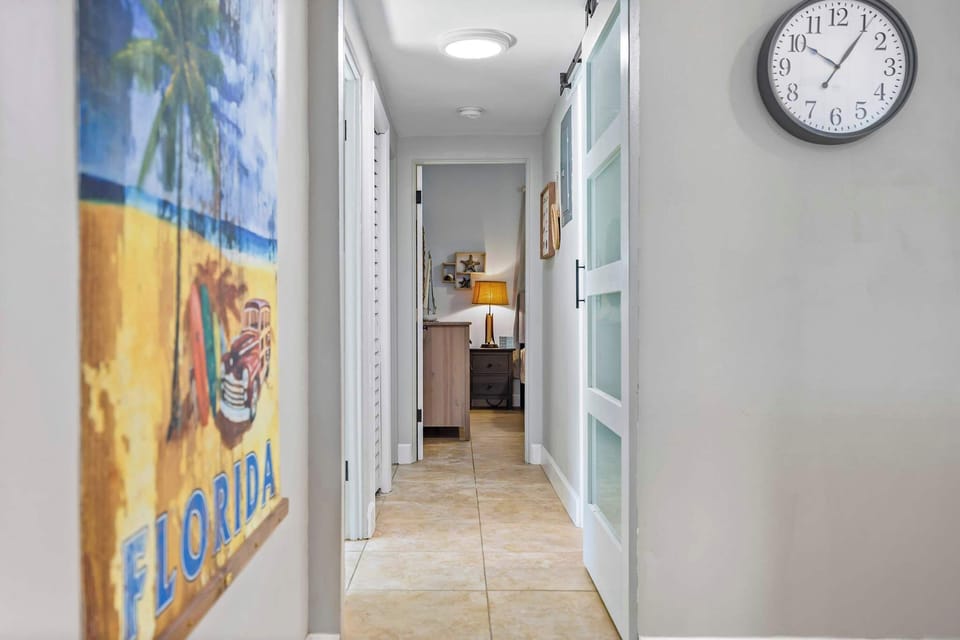 Bright hallway with tiled floors and coastal-themed decor leading to a bedroom.