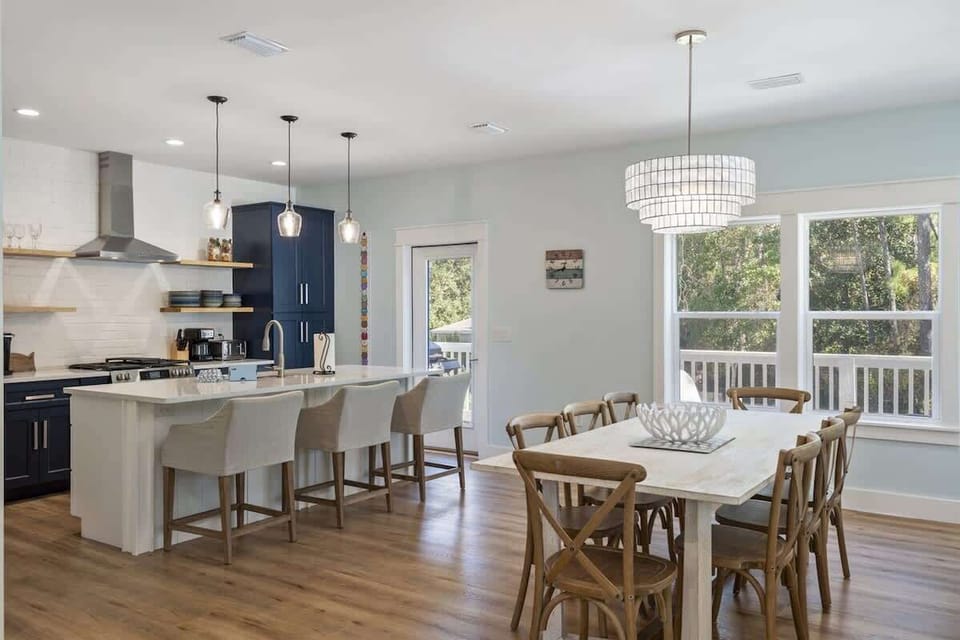 - Sunlit open concept dining area with large windows, natural wood floors, and modern charm - Elegant chandelier above a farmhouse style table, perfect for shared meals and memories - Seamless flow into the kitchen and out to the private deck