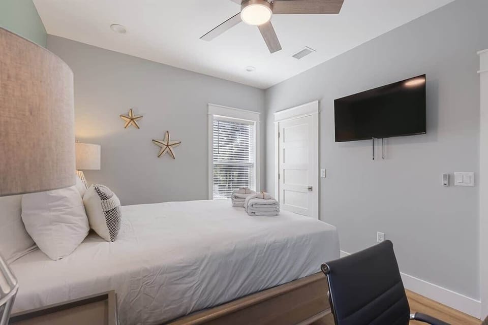 - Quiet bedroom with a cozy bed, plush bedding, and wall mounted TV for movie nights in bed - Decor includes a ceiling fan, reading lamps, and soft gray walls with natural accents - Large window brings in daylight while keeping the space cozy and cal