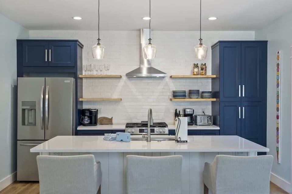 - Chef ready kitchen with sleek stainless steel appliances and navy cabinetry - Bright pendant lighting highlights a spacious island with bar seating for three - Open shelves, modern hood, and generous counter space blend style and function seamlessl