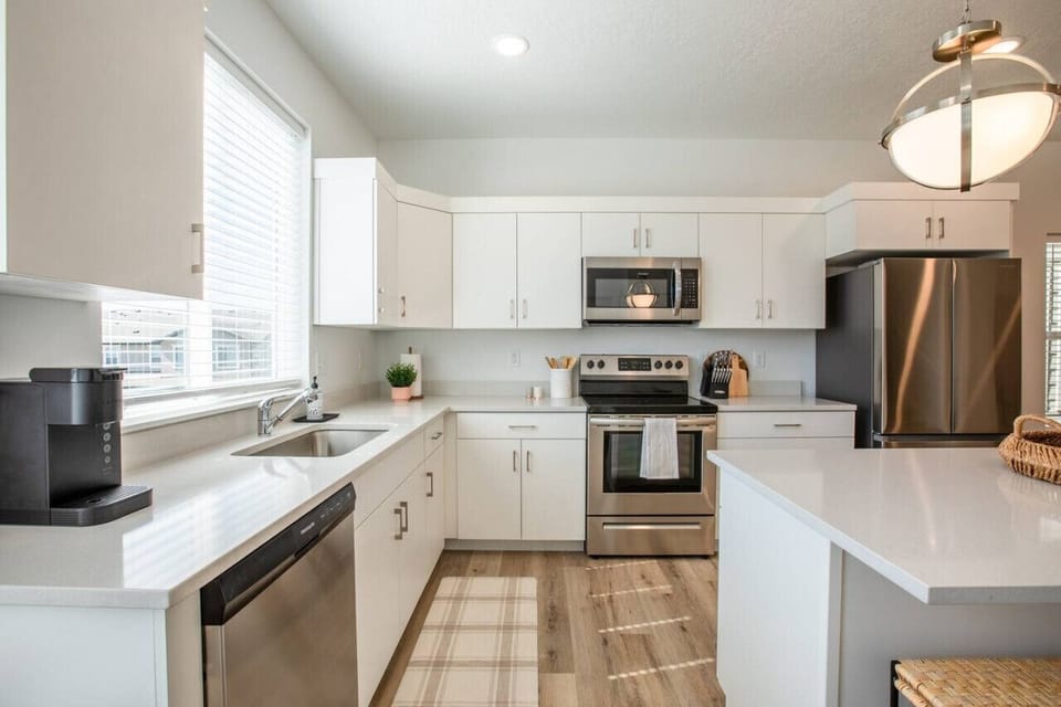 Fully equipped kitchen with stainless steel appliances, sleek white cabinetry, and a spacious island—perfect for preparing meals and connecting over breakfast.