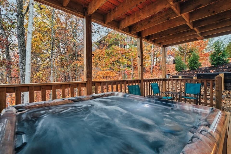 Covered outdoor hot tub with seating area overlooking autumn trees