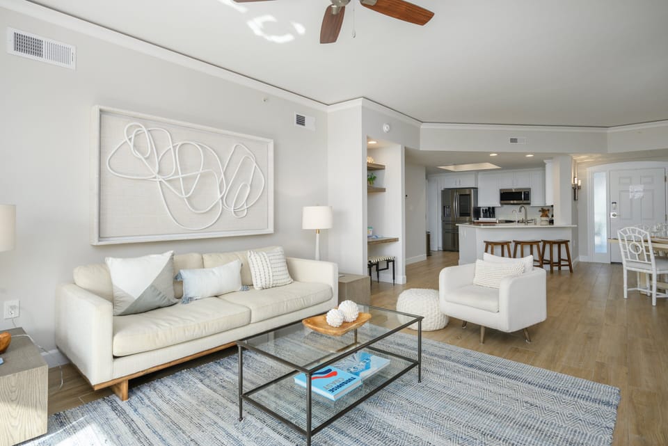 The open layout features neutral coastal tones, updated flooring, and modern furnishings that create a relaxed, beach-inspired atmosphere.
