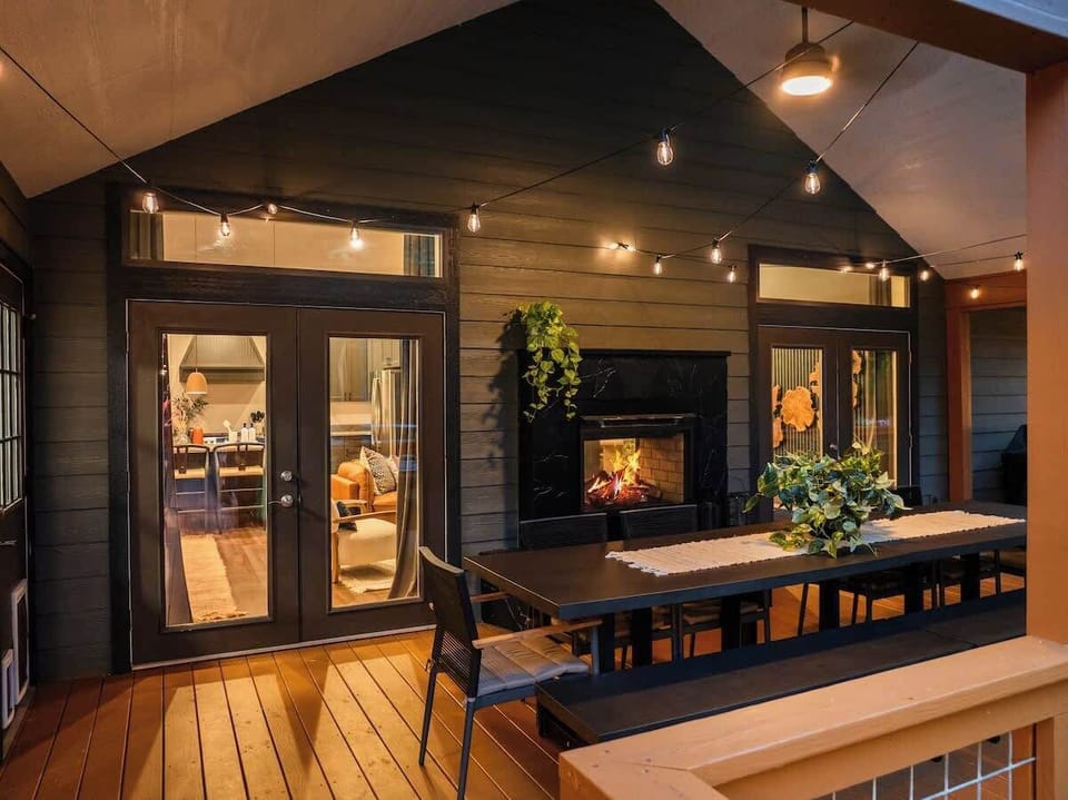 As night fall, the outdoor deck transforms into a cozy haven, illuminated by a fireplace and enchanting string lights, perfect for evening relaxation.
