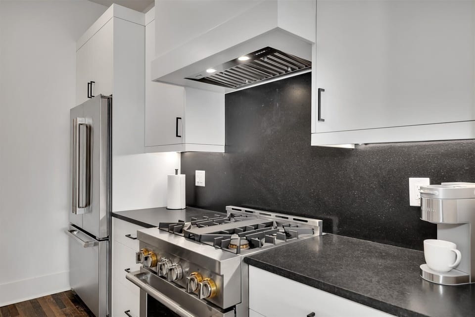Modern kitchen range w/ black backsplash, vent hood & sleek countertops