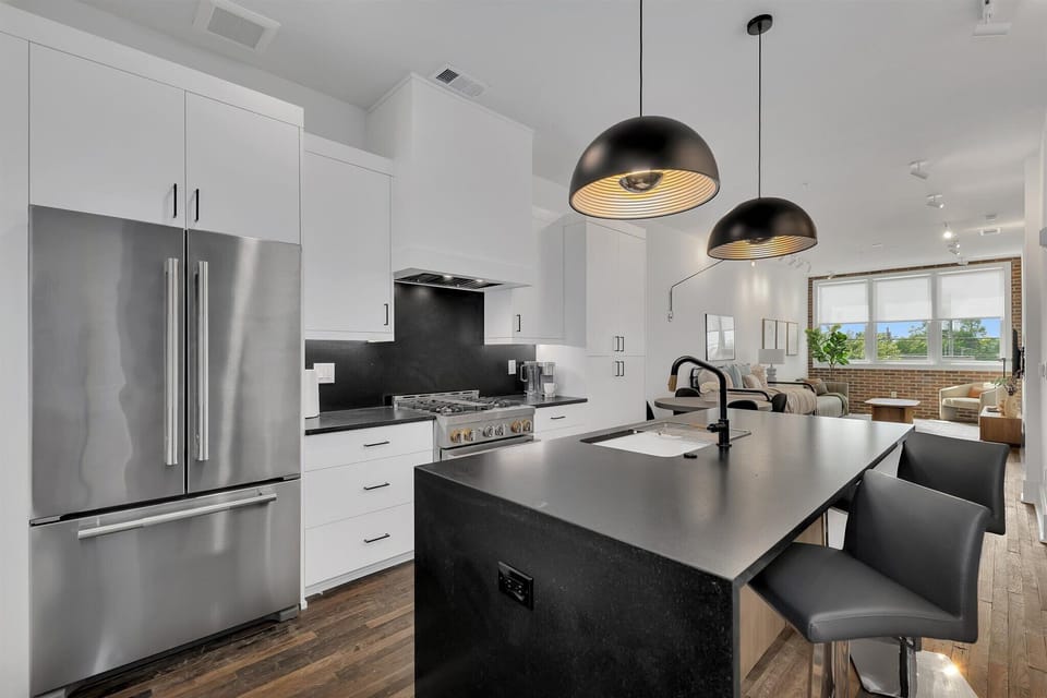 Sleek modern kitchen w/ black island, stainless steel appliances & pendant lighting
