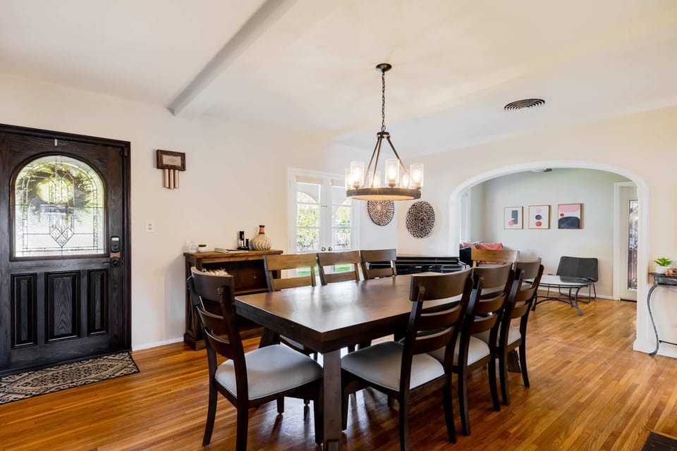 Dining room with hardwood floors, eight-seat table, pendant chandelier, and stained glass entry door - first impressions count