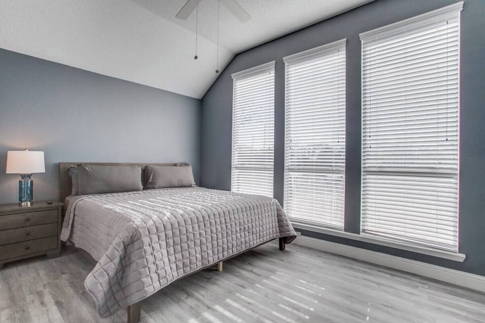 A comfortable guest bedroom offers a cushioned bed, neutral decor, and a wall of windows that brings in natural light.