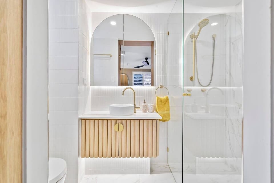 The modern ensuite bathroom off the primary features sleek gold-toned fixtures, a walk-in shower, and a luxurious design.