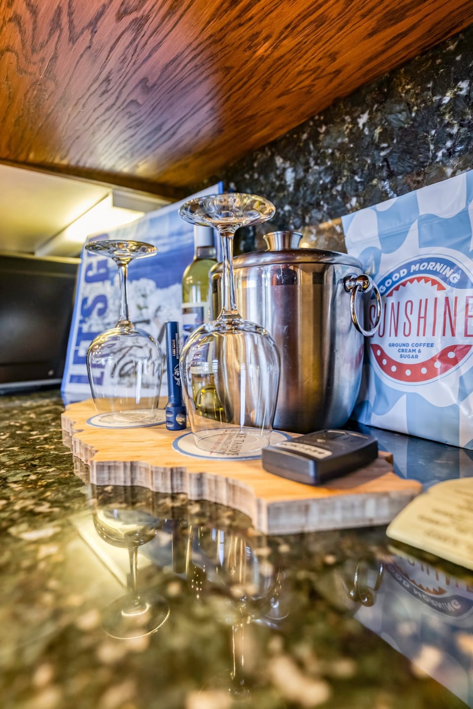 Kitchen counter with wine glasses, ice bucket, bottled wine, coffee bag, and remote controls.